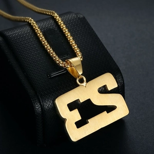 Détail du pendentif lettre DC doré avec texture en métal brossé et chaîne perle
