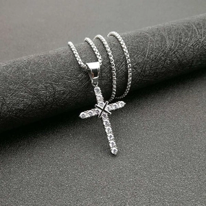 Macro view of a silver-toned cross pendant with cubic zirconia stones on a box chain