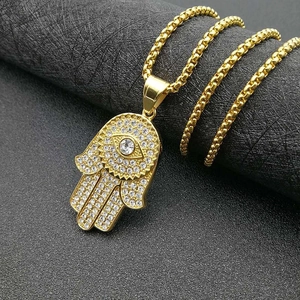 Collier avec pendentif main de Hamsa doré serti de zircons sur un fond noir texturé