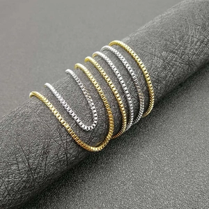 Gold and silver box chain necklaces displayed on a textured stand with a minimalist look