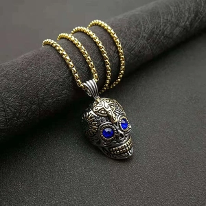 Détail d'un pendentif tête de mort punk aux yeux bleus sur chaîne box dorée