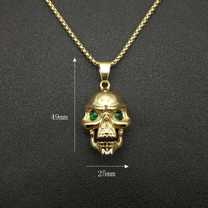 Pendentif crâne doré avec yeux verts et chaîne à maillons carrés sur fond sombre