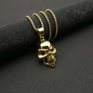 Collier tête de mort plaqué or avec yeux verts sur présentoir noir texturé
