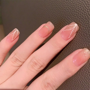 Peach pink press-on nails with white hand-painted leaf patterns and gold chain accents