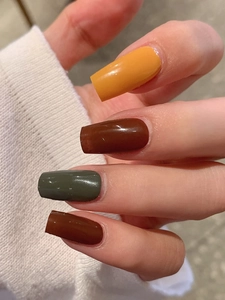 Detail of glossy coffin nail tips in mustard, chocolate, dark green, and mahogany shades