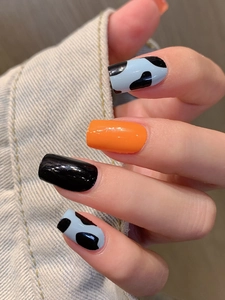 Detailed view of glossy orange and black press-on nails with blue cow print pattern