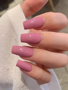 Close-up of dusty pink press-on nails with glitter finish in a long coffin shape