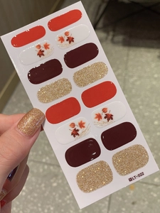 Detail view of autumn-themed maple leaf nail stickers with red color blocks and gold glitter