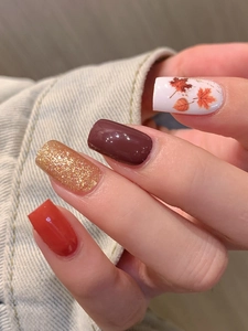 Close-up of autumn maple leaf nail stickers in dark brown and orange with gold glitter