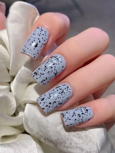 Detailed close-up of light blue rectangle press-on nails with black speckled egg texture