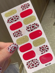 Detail of red leopard print nail stickers and gold glitter strips on human nails