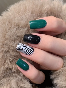 Close-up of glossy dark green and black nails with artistic zebra patterns