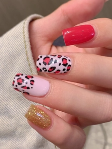 Close-up of red and leopard print press-on nails with gold glitter on denim background