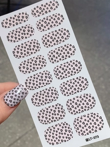 Detail of pink nail stickers with black heart patterns showing application on fingernail