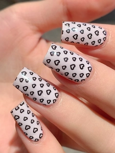Close-up of pink self-adhesive nail wraps with black heart patterns on short oval nails