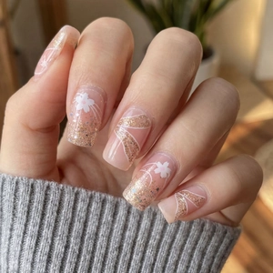 Pink press-on nails with white floral patterns and gold glitter in a long coffin shape