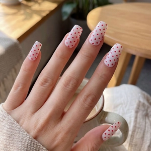 Minimalist white press-on nails with red heart pattern shown on hands holding a cup