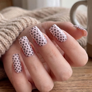 Minimalist pink press-on nails with black heart patterns and square oval shape