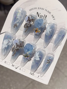 Close-up of handmade ice blue press-on nails with 3D butterflies and floral details
