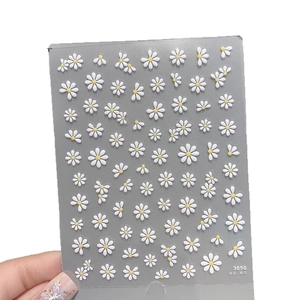 3D embossed white daisy nail stickers with yellow centers on a grey-blue card board