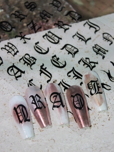 Macro shot of Gothic Old English nail stickers with black lettering on rose gold press-ons
