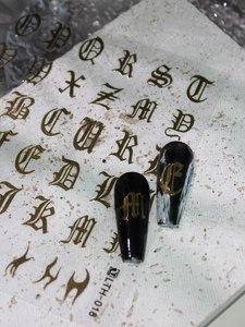 Macro shot of gold Gothic letter nail stickers applied on glossy black long nails