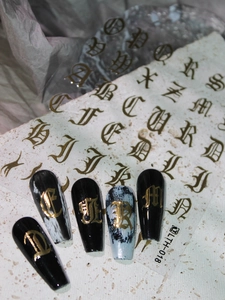 Detailed view of gold gothic letter nail art stickers applied on black manicure tips