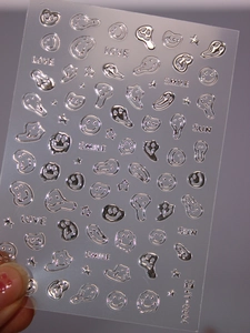 Close-up of silver reflective nail stickers with melting smiley face and star patterns