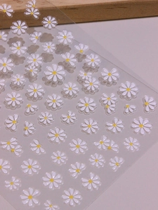 Macro view showing 3D embossed texture of white daisy nail stickers with yellow centers