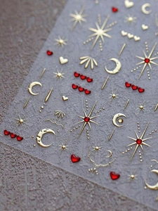 Macro shot of gold foil moon and star nail stickers with red hearts on a stone surface