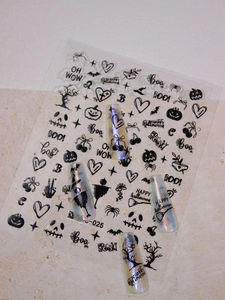 Detail of Halloween nail stickers with black ghosts, pumpkins and bats on blue nails