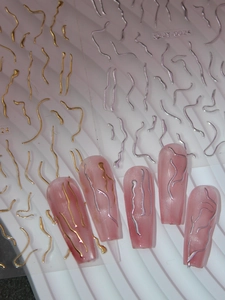 Macro detail of 3D embossed gold and silver metallic line stickers on pink nails