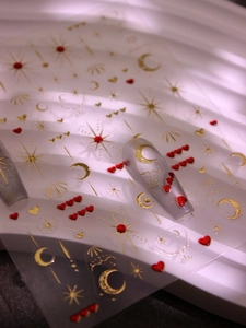 Macro shot of 3D gold moon and star nail stickers with red heart rhinestone detail