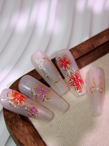 Détail de nail art floral 5D avec lignes métalliques dorées et perles sur base rose