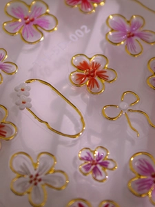 Détail macro de stickers 5D en relief pour ongles avec fleurs et bordures dorées