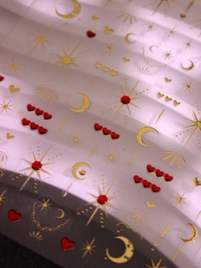Macro view of 3D gold stars, moons, and red hearts embossed on nail art stickers