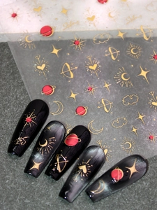 Macro detail of gold foil celestial nail stickers with stars and moon on black nails