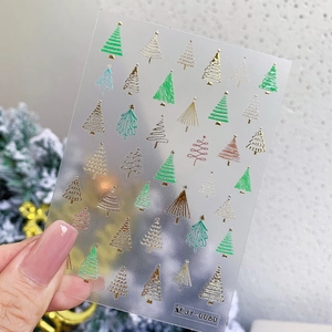 Close-up of gold Christmas tree nail decals with fine glitter details and 3D texture