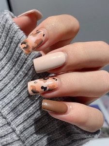 Macro view of leopard print and solid brown press-on nails on gray knitted fabric