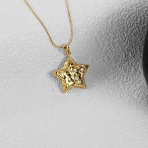Collier pendentif étoile dorée avec texture martelée et trois perles sur fond gris