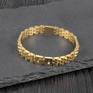 Macro shot of gold stainless steel watch-style link bracelet on dark stone texture