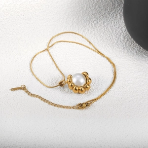Détail d'un pendentif doré en forme de C avec perle d'imitation sur une chaîne serpent