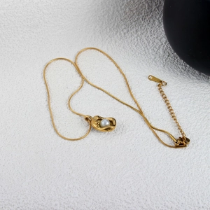 Detail of a gold necklace featuring an irregular lava-textured metal pendant with a white pearl
