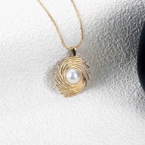 Elegant gold swirling vortex pendant necklace with a white pearl on white stone surface
