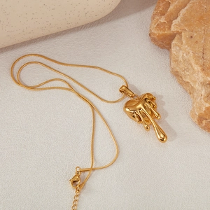 Détail du pendentif cœur de lave doré sur chaîne serpent sur fond de pierre texturée