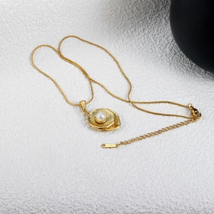Detail of gold stainless steel necklace with oval sunburst pendant and white pearl inlay
