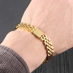 Gold stainless steel watch-band style bracelet for men on a wrist with wood background