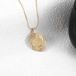 Elegant gold spiral pendant necklace with textured finish on a minimalist stone background