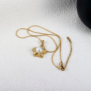 Détail d'un pendentif étoile de mer doré avec perle centrale sur chaîne serpent