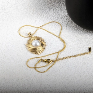 Detail of gold snake chain necklace with spiral swirl pendant and central white pearl